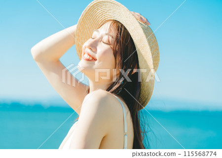A woman wearing a straw hat with the sea and blue sky in the background A woman wearing a straw hat with the sea and blue sky in the background 115568774