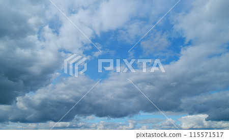Blue clear sky with white cumulus and cirrus on different layers spindrift clouds background. Light white cirrus clouds in blue sky on a summer day. Timelapse. 115571517