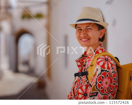 Nice asian Female in boho dress Enjoying Sunny Day on Greek Islands. Travel to Lindos, Mediterranean islands tourist season. Tourist woman on vacation in Greece walking through the streets of Lindos. 115572426