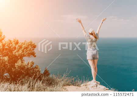 Woman travel sea. Happy tourist in hat enjoy taking picture outdoors for memories. Woman traveler posing on the beach at sea surrounded by volcanic mountains, sharing travel adventure journey 115572471