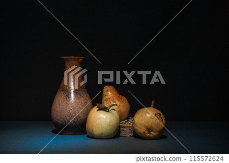 Empty vintage brown ceramic vase and next to them green apple and two bears on a rustic wood on a black background. Still life, plenty of space for text. 115572624