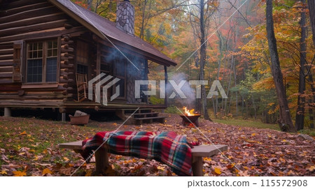 A cozy log cabin nestled in the woods with a fire pit burning in front of the porch 115572908