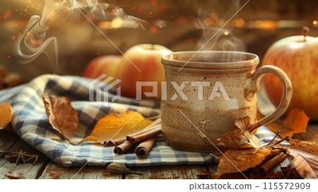 A rustic scene of a steaming mug of hot apple cider resting on a checkered blue and white cloth 115572909