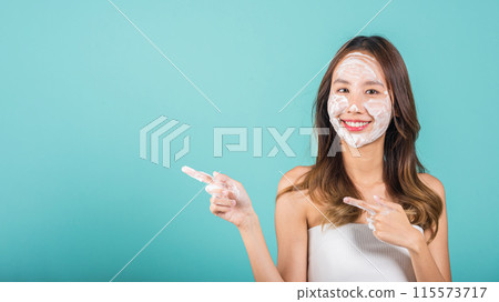 Portrait Asian young woman washing face foaming facewash soap scrub on skin studio shot isolated on blue background, female applying bubble facial foam and cleansing and pointing finger to side away Portrait Asian young woman washing face foaming facewash soap scrub on skin studio shot isolated on blue background, female applying bubble facial foam and cleansing and pointing finger to side away 115573717