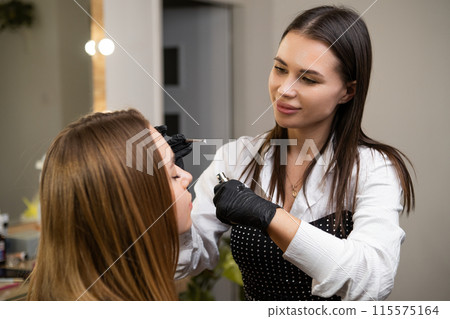 A woman receives a brow lamination treatment from a professional at beauty salon 115575164