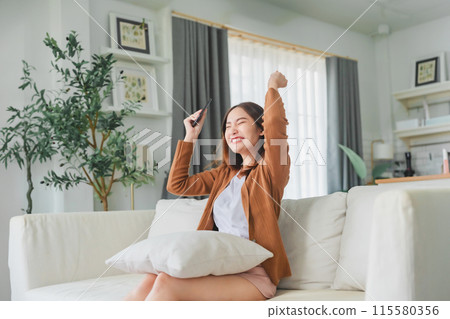 Happy young asian woman relax on comfortable couch at home texting messaging on smartphone 115580356