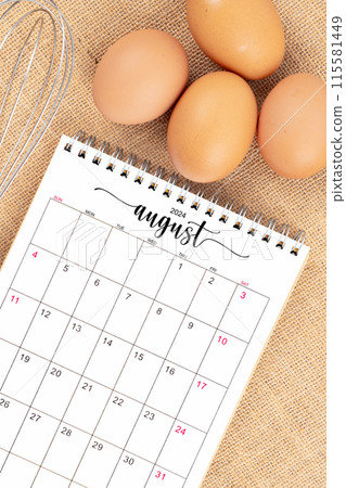 August 2024 Desk calendar and fresh eggs with egg whisk on burlap background. August 2024 Desk calendar and fresh eggs with egg whisk on burlap background. 115581449