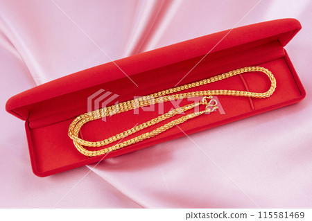 Gold Necklace in red velvet box container on pink fabric background. 115581469