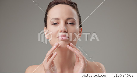 Beauty, health, cosmetics, anti-aging therapy and skin care concept - young beautiful brunette Caucasian woman touching face and looking at camera Beauty, health, cosmetics, anti-aging therapy and skin care concept - young beautiful brunette Caucasian woman touching face and looking at camera 115584562