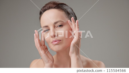 Beauty, health, cosmetics, anti-aging therapy and skin care concept - young beautiful brunette Caucasian woman touching face and looking at camera Beauty, health, cosmetics, anti-aging therapy and skin care concept - young beautiful brunette Caucasian woman touching face and looking at camera 115584566