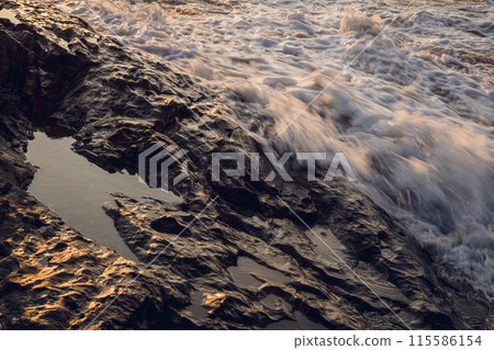 A large rocks surrounded by waves of the ocean A large rocks surrounded by waves of the ocean 115586154