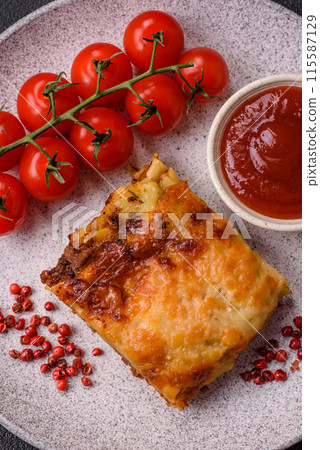 Delicious baked lasagna pasta with meat, sauce, salt, spices and herbs on a dark concrete background Delicious baked lasagna pasta with meat, sauce, salt, spices and herbs on a dark concrete background 115587129