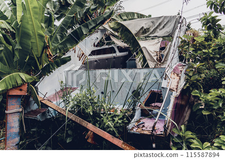 Old and rusty motor boats on a landfill surrounded by tropical forest 115587894