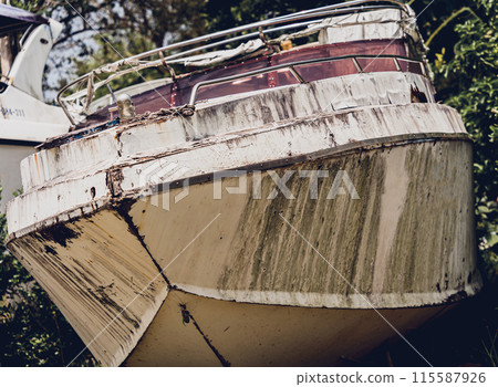 Old and rusty motor boats on a landfill surrounded by tropical forest 115587926