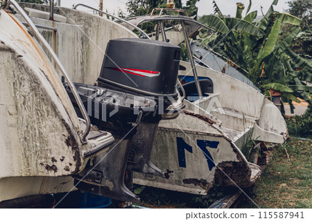 Old and rusty motor boats on a landfill surrounded by tropical forest 115587941