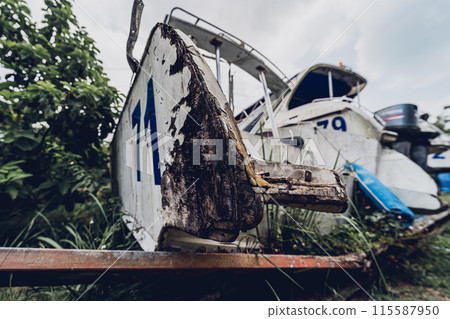 Old and rusty motor boats on a landfill surrounded by tropical forest 115587950