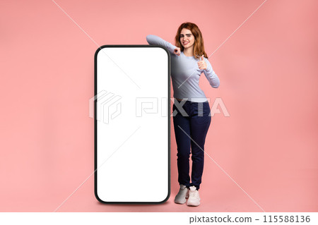 Smiling woman showing thumbs up near huge cellphone with blank screen 115588136