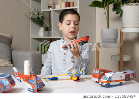 The child makes crafts from paper, glue and scissors. Childrens creativity, interesting leisure The child makes crafts from paper, glue and scissors. Childrens creativity, interesting leisure 115588484