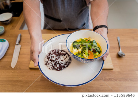 Chef at the kitchen preparing green curry with herbs and rice 115589646