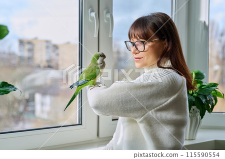 Middle aged woman and parrot together at home, near winter window 115590554