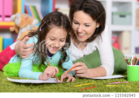 Portrait of little cute girl with mother drawing lying on green carpet 115592045