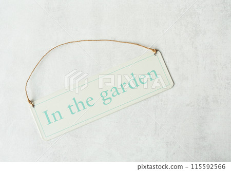 A pastel green sign with In the garden text, hanging by a twine string on a textured white background. 115592566