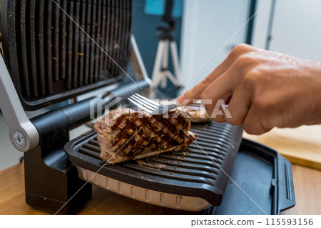 Chef at the kitchen preparing beef steaks on the home electric grill 115593156