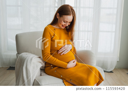 Pregnancy motherhood people expectation future. Pregnant woman with big belly sitting on chair near window at home. Girl hugging her tummy enjoying pregnancy. Maternity tenderness parenthood new life 115593420