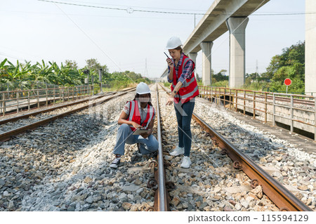 Rail transportation engineer in safety vest and hardhat check the neatness of the railway track while holding walkie-talkie and tablet computer. Rail transportation engineer in safety vest and hardhat check the neatness of the railway track while holding walkie-talkie and tablet computer. 115594129
