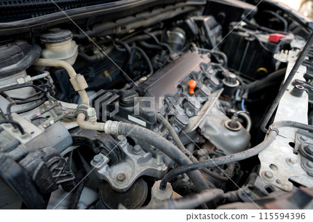 Closeup view of a car engine with various component and wire visible under the hood. Closeup view of a car engine with various component and wire visible under the hood. 115594396