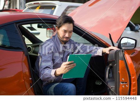 A mechanic in work uniform with a document clipboard, smile while inspect a car coming for maintenance at a repair shop. 115594448