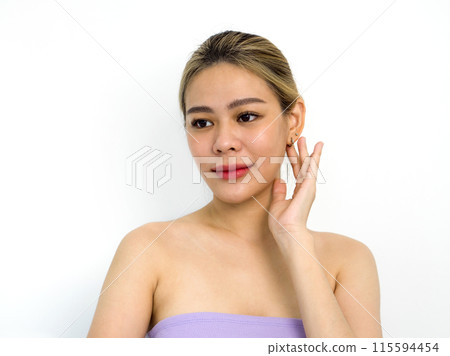 A woman with blonde hair in a purple top gently touching her ear. Portrait on white background with studio lighting. 115594454