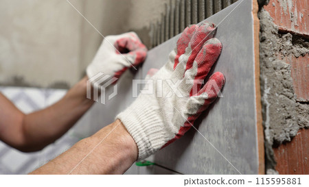 Instaling ceramic tiles. Male hands glue ceramic tiles on the wall in the bathroom. Instaling ceramic tiles. Male hands glue ceramic tiles on the wall in the bathroom. 115595881