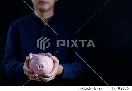 Man hands hold a pink piggy bank with black background. The concept of saving money, investment 115595970