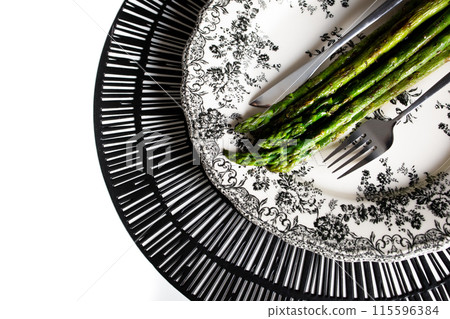 Cooked roasted asparagus and cutlery on white plate with black floral print Cooked roasted asparagus and cutlery on white plate with black floral print 115596384