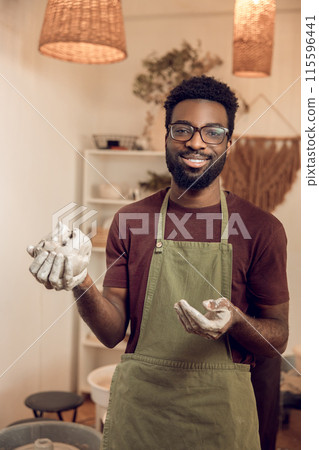 African american smiling sculptor with wet clay in hands looking contented 115596441