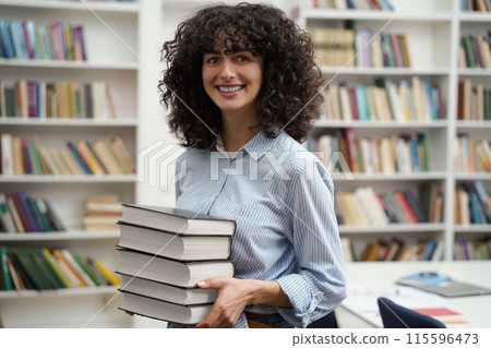 Pretty woman carrying a pile of books and smiling nicely 115596473