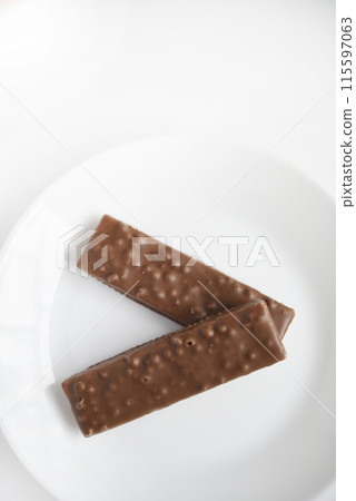 A sweet chocolate bar on a white plate.Waffle chocolate bar on a white background. A sweet chocolate bar on a white plate.Waffle chocolate bar on a white background. 115597063