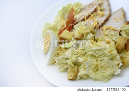 Caesar salad with meat and vegetables on a white plate. Light breakfast with egg, meat and vegetables. Caesar salad with meat and vegetables on a white plate. Light breakfast with egg, meat and vegetables. 115598492