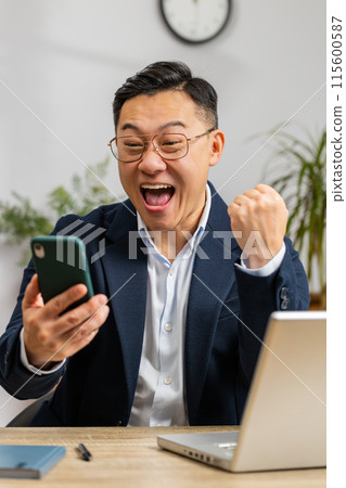 Happy Asian businessman use smartphone celebrating success victory, winning, play online game 115600587