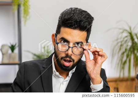 Businessman working at home office taking off glasses, shocked by sudden victory, lottery winning 115600595