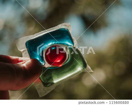 Laundry detergent pod. Men hand holds colorful water soluble sachet. Packs or liquitabs are water-soluble pouches containing highly concentrated laundry detergent, softener and other laundry products Laundry detergent pod. Men hand holds colorful water soluble sachet. Packs or liquitabs are water-soluble pouches containing highly concentrated laundry detergent, softener and other laundry products 115600880