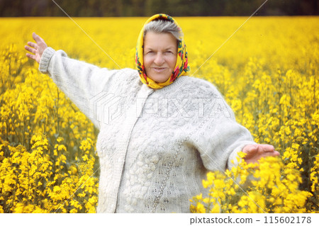 An old woman in yellow headcrarf and purple scirt enjoying a walk in the open air. 115602178