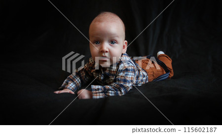 A baby in mustard pants and a plaid shirt lies on a black background. 115602187