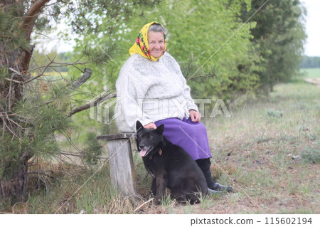 Elderly grayhaired in yellow headskarf woman with her lovely black dog in the park.  115602194