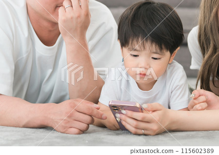 Asian boy playing videos and games on his smartphone in the living room Asian boy playing videos and games on his smartphone in the living room 115602389