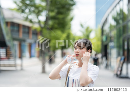 A young and cute Japanese woman hydrates while wiping sweat with a towel outdoors | Heat stroke prevention image | Hydration image 115602413