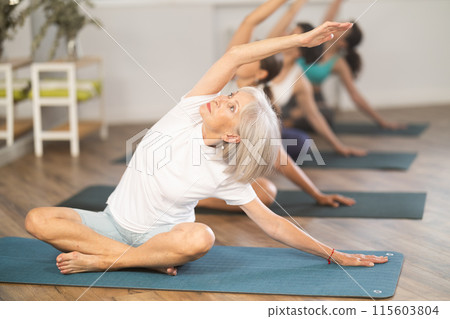 Senior woman performing side stretch in easy pose at yoga class Senior woman performing side stretch in easy pose at yoga class 115603804