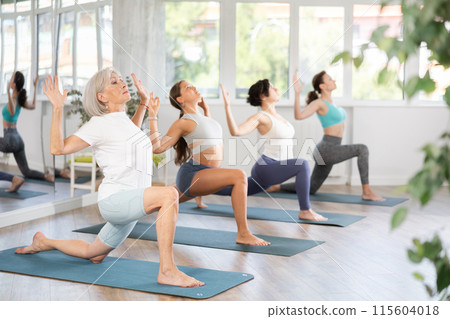 Woman standing yoga pose and making full body stretching workout with group in room 115604018