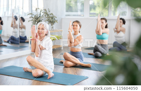 Positive elderly woman performing Gomukhasana Garudasana in yoga studio Positive elderly woman performing Gomukhasana Garudasana in yoga studio 115604050